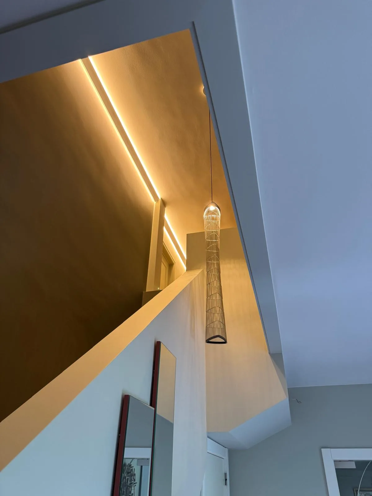 Trapgat met verticale LED-lijnverlichting in het plafond en een cilindervormige design-hanglamp met vlechtpatroon