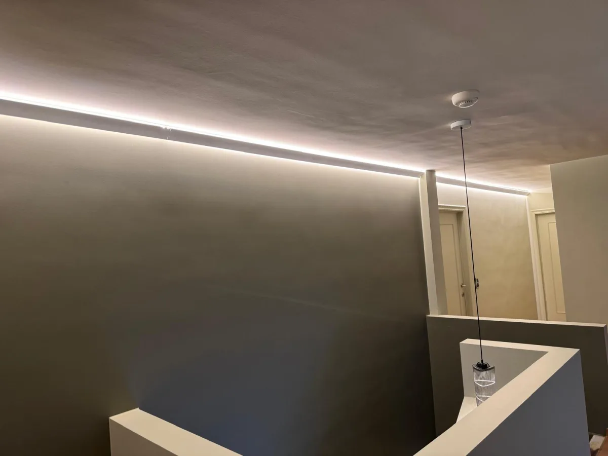 Lange gang met ingewerkte LED-lijnverlichting langs plafond en muur, met design-hanglamp